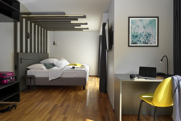 A modern hotel room with a bed, a desk with a laptop, a chair, and a TV.