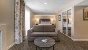 A hotel room with a bed, a sofa, a coffee table, and a large window with curtains. - Chase Suite Hotel El Paso (El Paso)