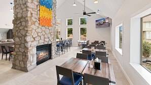 A spacious indoor dining area with a stone fireplace, multiple tables and chairs, large windows, and a ceiling fan. - Chase Suite Hotel El Paso (El Paso)