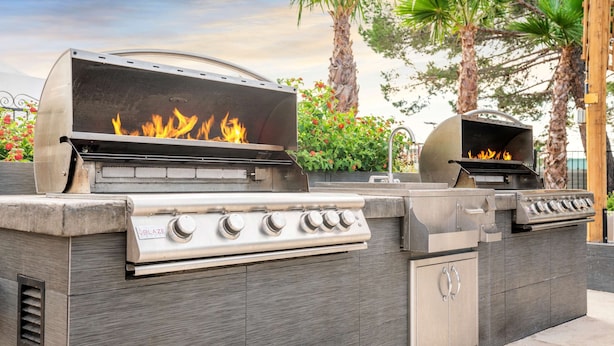 A barbecue grill with a built-in oven and a separate grill area, both with visible flames. - Chase Suite Hotel El Paso (El Paso)