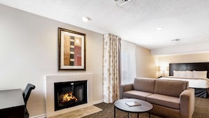 A hotel room with a fireplace, a sofa, a bed, and a desk. - Chase Suite Hotel El Paso (El Paso)