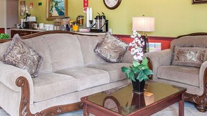 A living room with a sofa, a coffee table, a clock, and a painting on the wall. - Econo Lodge Dexter (Dexter)