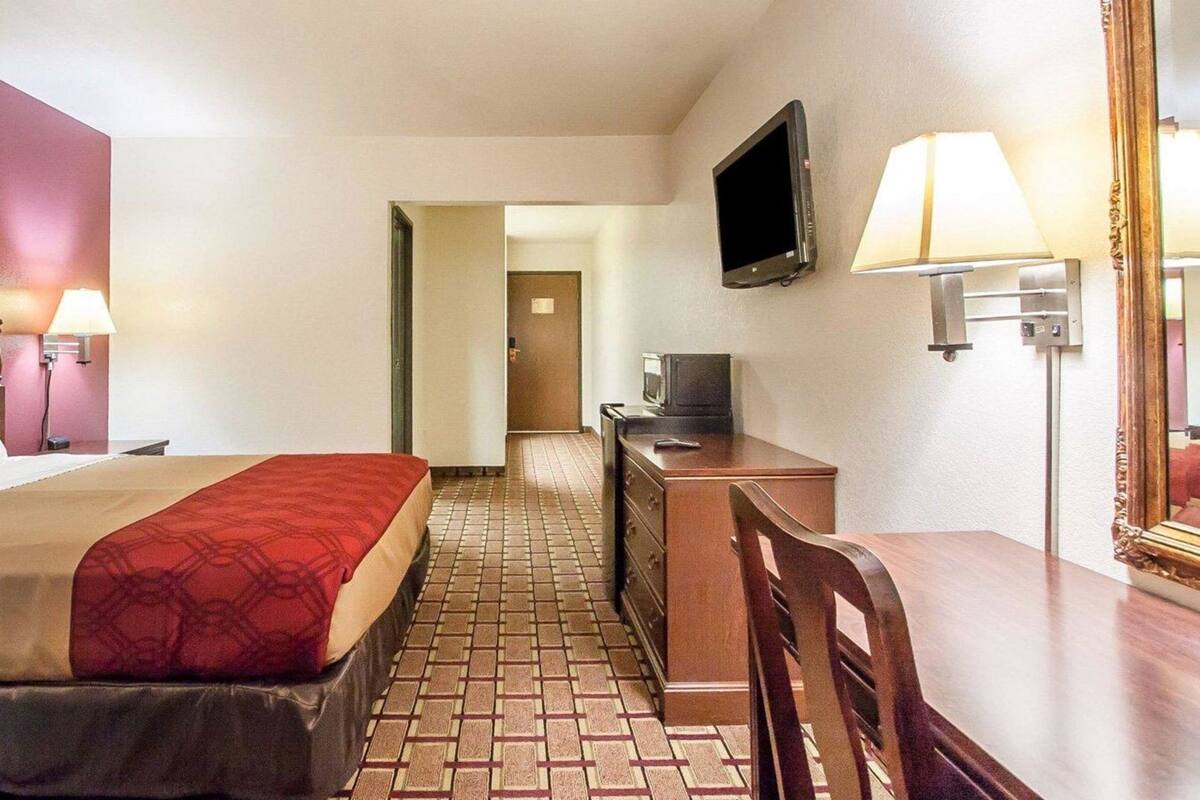 A hotel room with a bed, a desk, a television, a mirror, and a lamp.