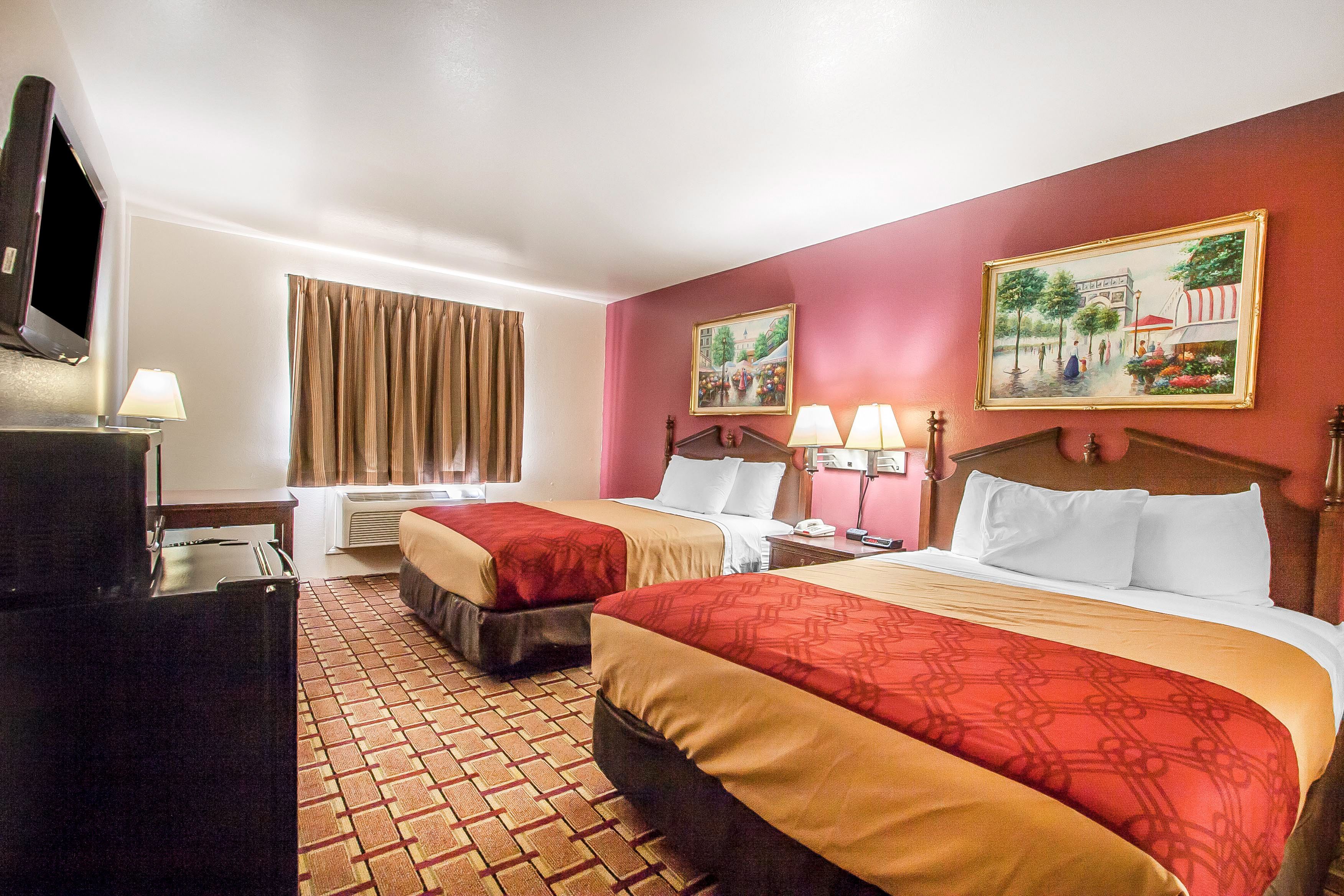 A hotel room with two beds, a TV, a desk, and a window with curtains.