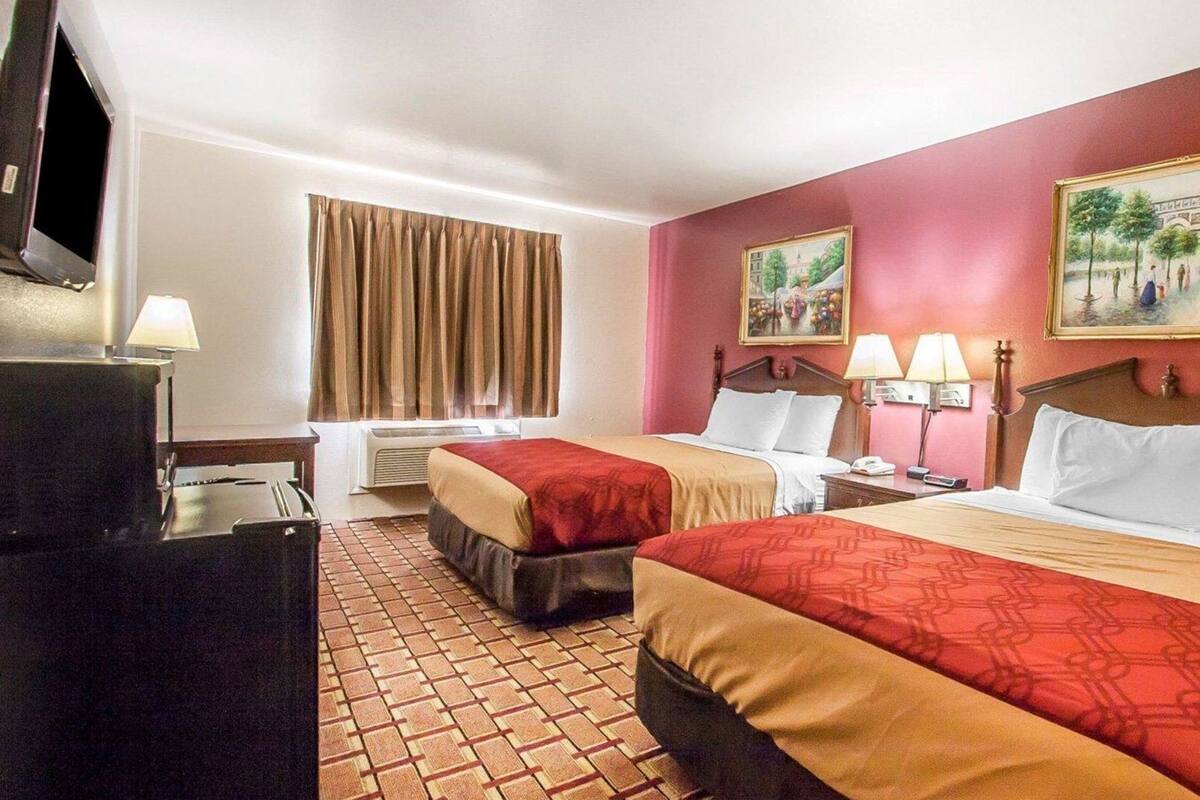 A hotel room with two beds, a television, a desk, and a window with curtains.
