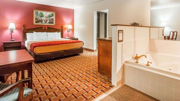 A hotel room with a bed, a desk, a chair, a bathroom with a bathtub, and a patterned floor. - Econo Lodge Dexter (Dexter)