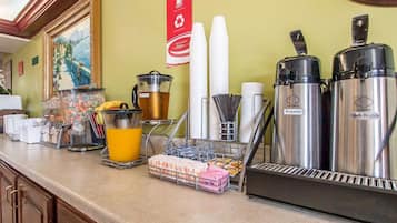 A hotel breakfast bar with coffee makers, a fruit dispenser, and a juice cooler.
