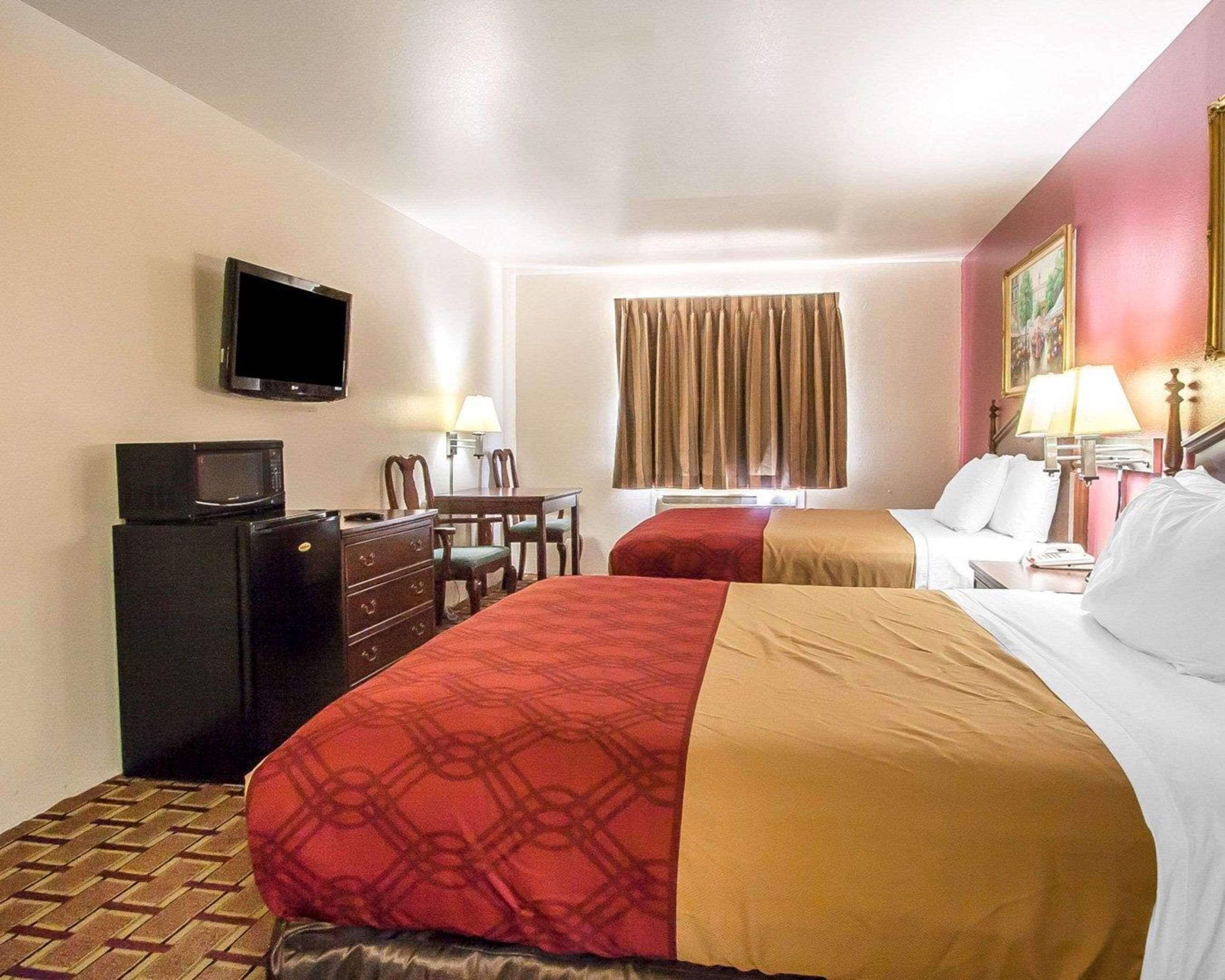 A hotel room with two beds, a desk with a chair, a television, and a window with curtains.