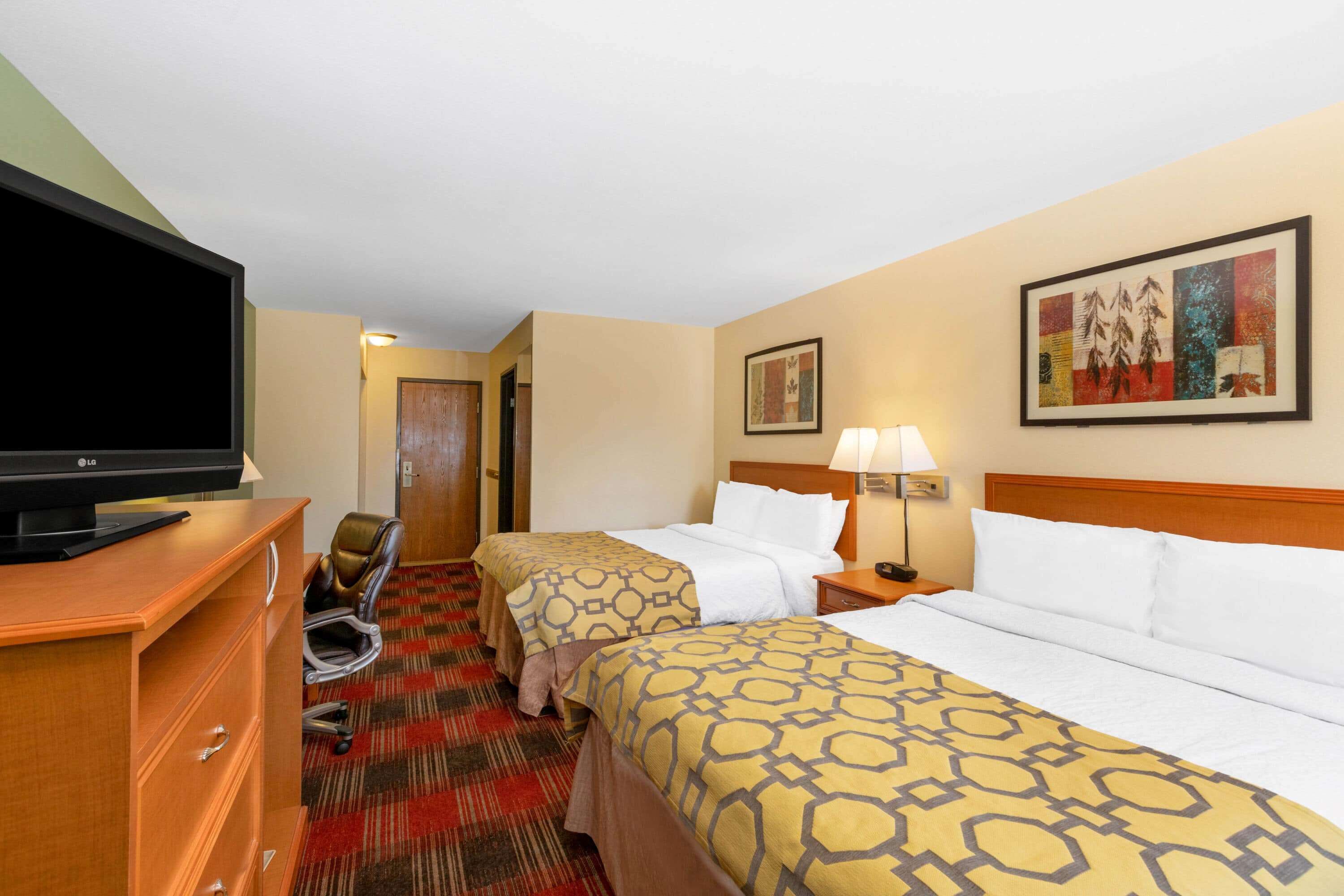 A hotel room with two beds, a TV, a desk, and a chair.
