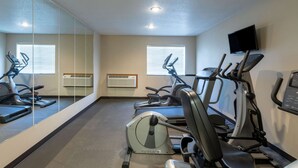 Un gimnasio con equipo de ejercicio, un espejo grande y un televisor en la pared.