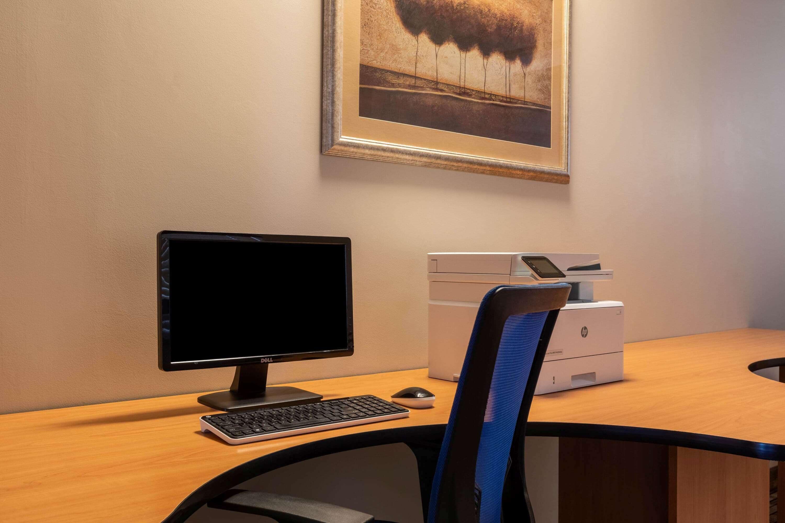 Una scrivania con un monitor computer, tastiera, mouse, una stampante e una sedia con schienale blu.
