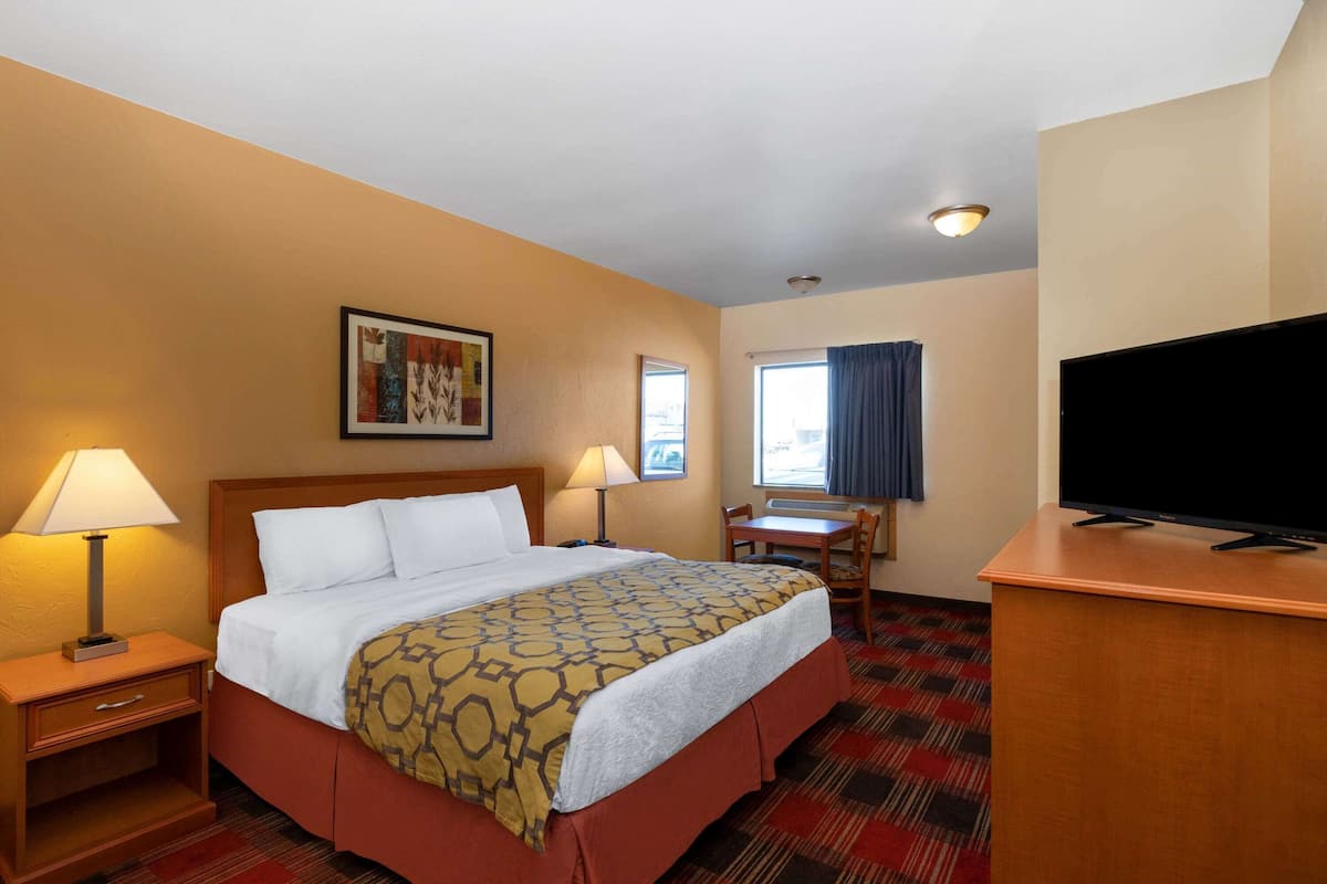Een hotelkamer met een bed, twee nachtkastjes met lampen, een bureau met stoel, een flatscreen televisie en een raam met gordijnen.