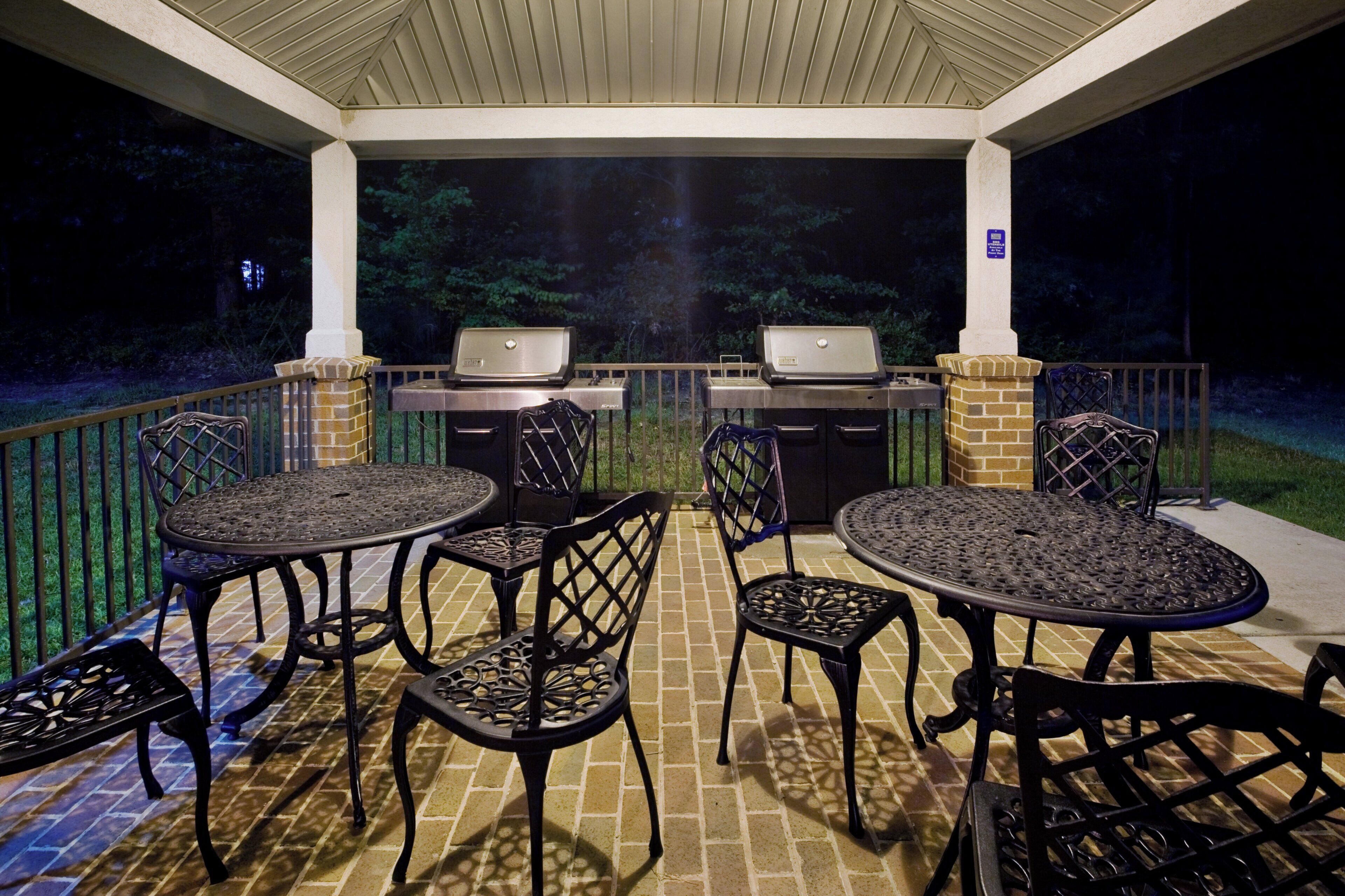 An outdoor patio with two barbecue grills, four chairs, and a table.