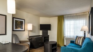 Une chambre d’hôtel moderne équipée d’une télévision à écran plat, d’un bureau avec un téléphone, d’un canapé bleu et d’une petite table ronde.