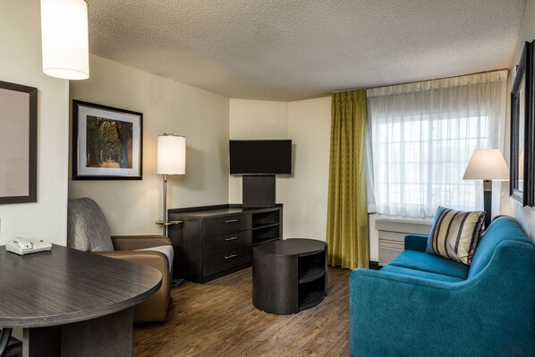 Ein modernes Hotelzimmer mit einem Flachbildfernseher, einem Schreibtisch mit Telefon, einem blauen Sofa und einem kleinen runden Tisch.