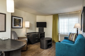 Une chambre d’hôtel équipée d’un téléviseur à écran plat, d’un bureau avec un téléphone, d’un canapé et d’une petite table ronde.