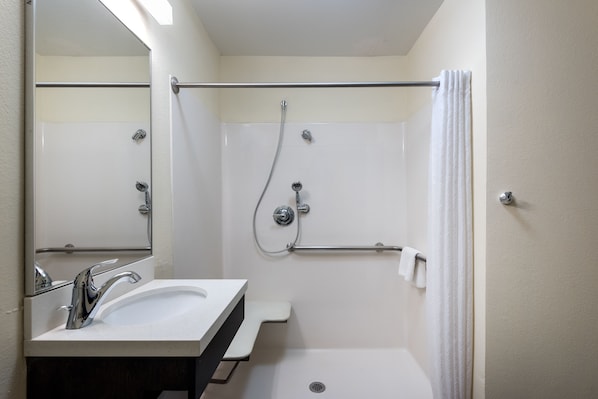 Un baño con lavamanos, espejo, ducha y toallero.