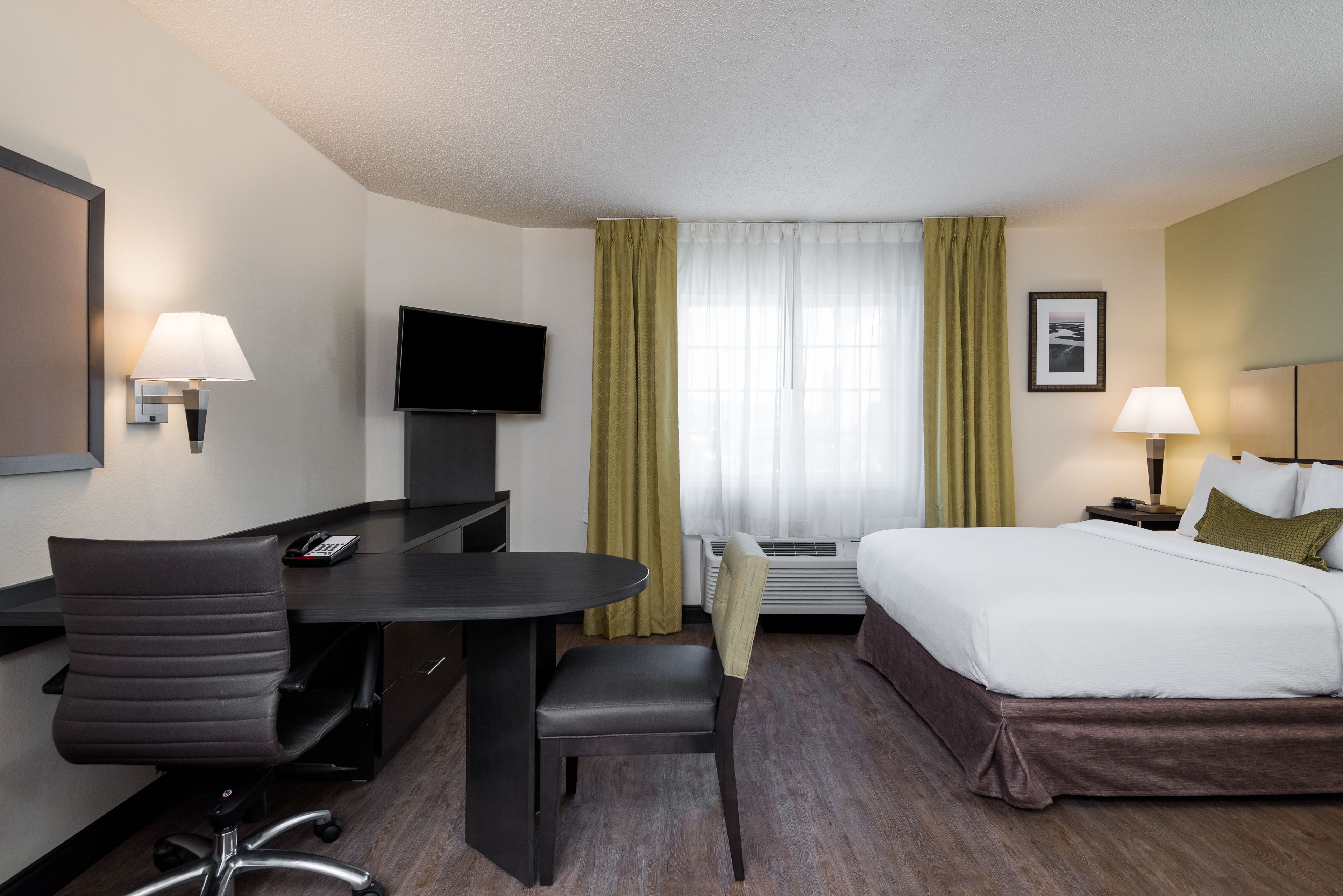 A hotel room with a bed, a desk with a chair, a TV, and a window with curtains.