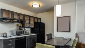 Una cocina compacta con microondas, estufa y refrigerador. Hay una mesa de comedor con sillas y una lámpara colgante.