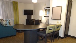 Un espace de vie compact comprenant une table à manger, deux chaises, un canapé, un téléviseur, une lampe et un réfrigérateur.
