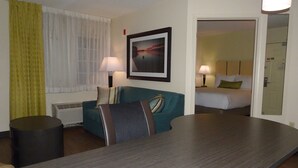 Une chambre d’hôtel avec une table à manger en bois, un canapé bleu, un lit avec une literie blanche et un tableau encadré au mur.
