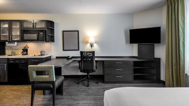 Una habitación de hotel con kitchenette, escritorio, silla, televisión y cama.