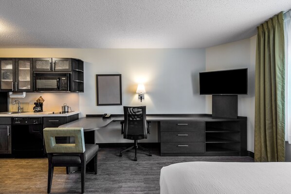 Ein Hotelzimmer mit Küchenzeile, Schreibtisch, Stuhl, Fernseher und Bett.