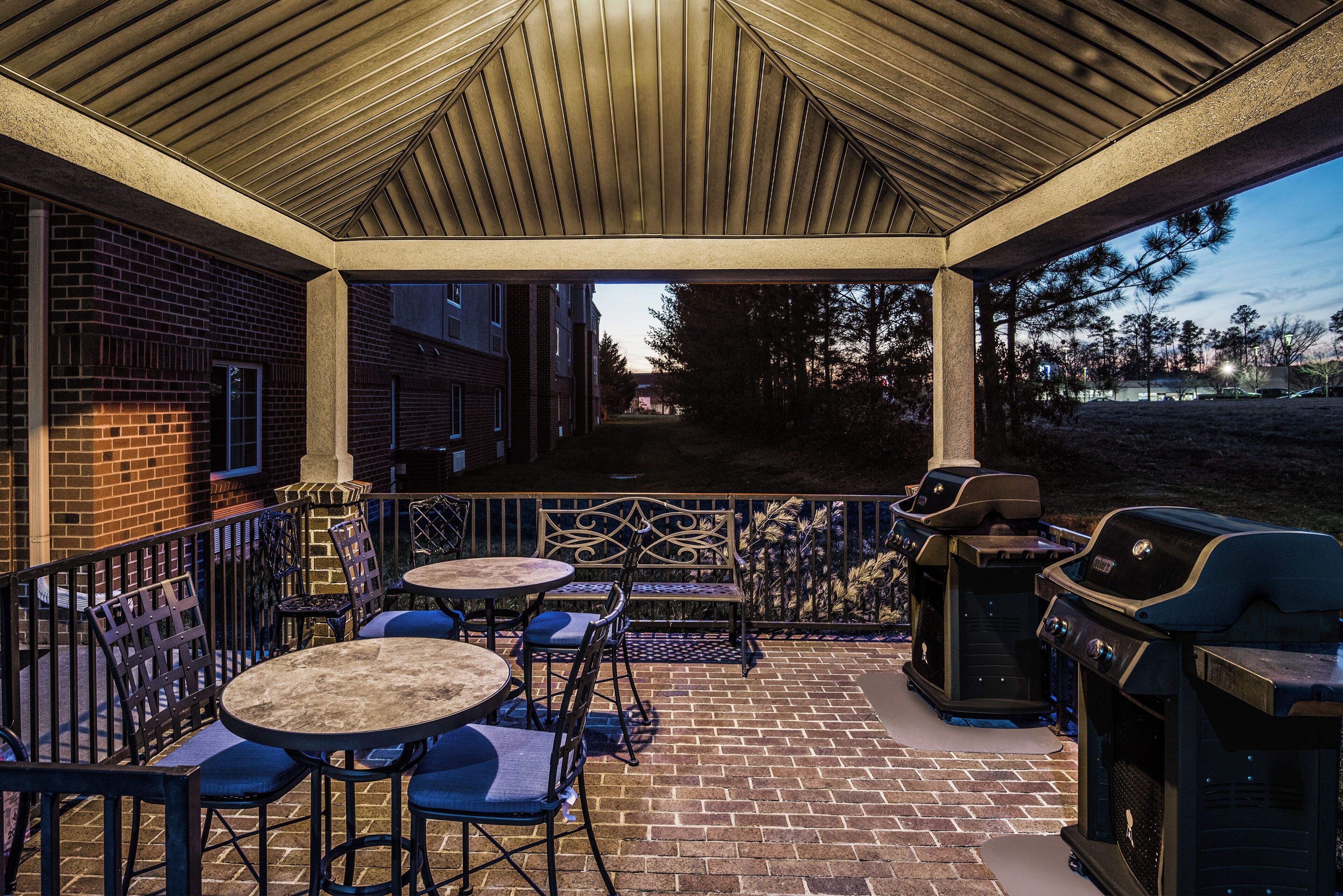 Une terrasse extérieure avec un sol en briques, une clôture en métal et un barbecue.