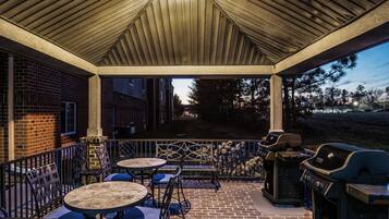 Une terrasse extérieure avec un sol en briques, une clôture en métal et un barbecue.