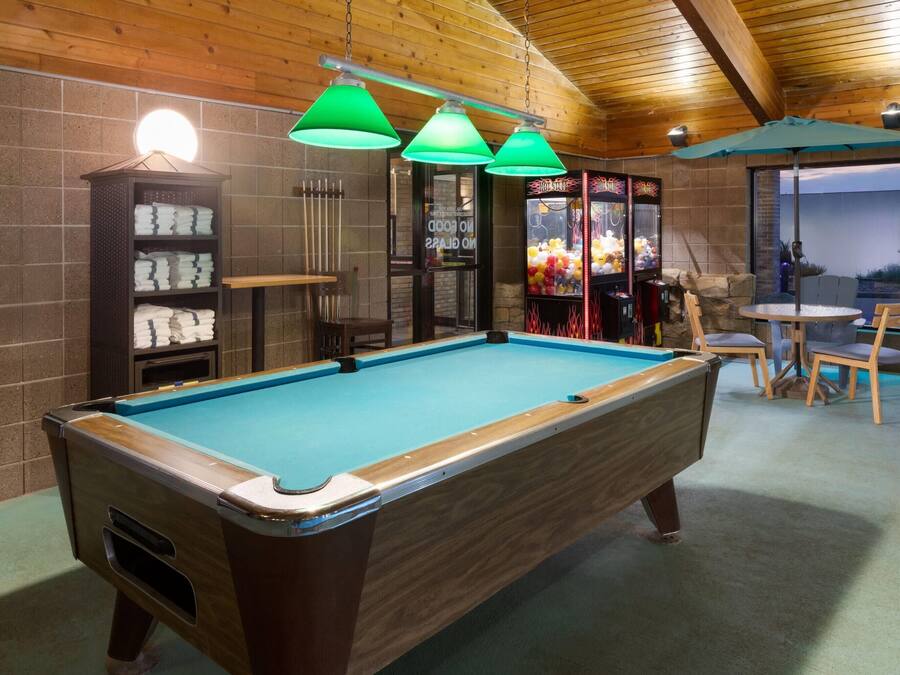 A pool table with three hanging lamps, a pool cue rack, and a seating area with chairs and a table.