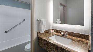 Un baño con una bañera blanca, un lavabo con encimera de granito y un espejo sobre el lavabo.