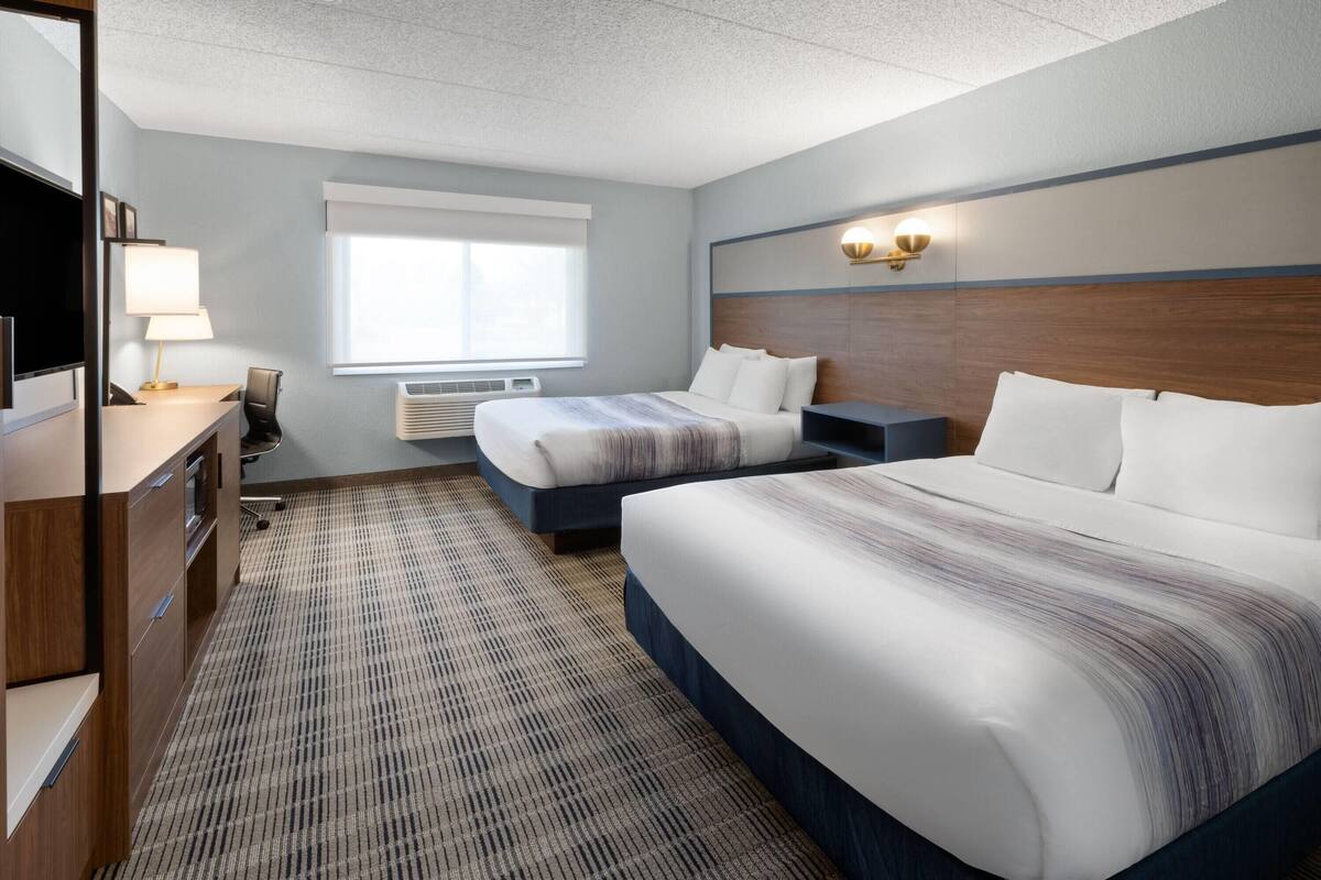 A hotel room with two beds, a desk, a chair, a TV, and a window with blinds.