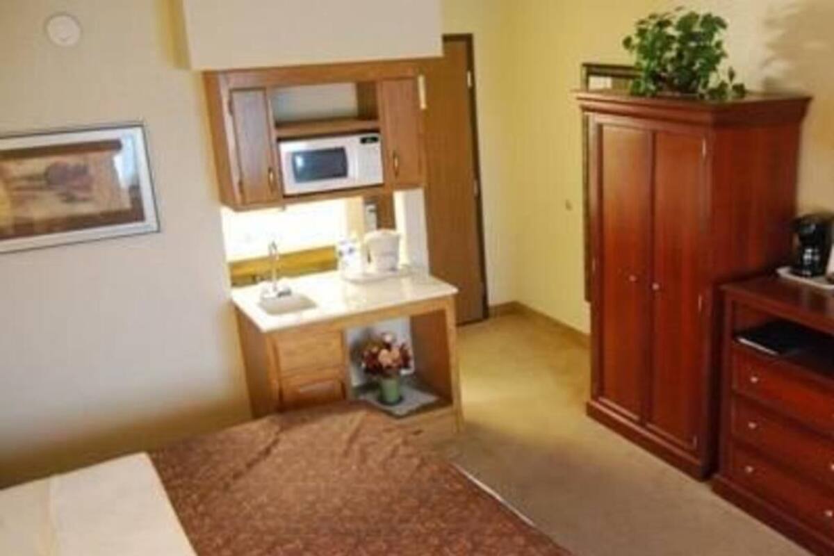 A compact room with a bed, a kitchenette with a microwave, a sink, and a cabinet.