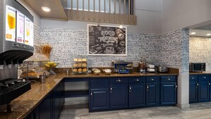 A modern kitchen with dark blue cabinets, a granite countertop, and a backsplash made of small tiles. There is a large chalkboard with "Good Morning" written on it, and various kitchen appliances and utensils are visible.