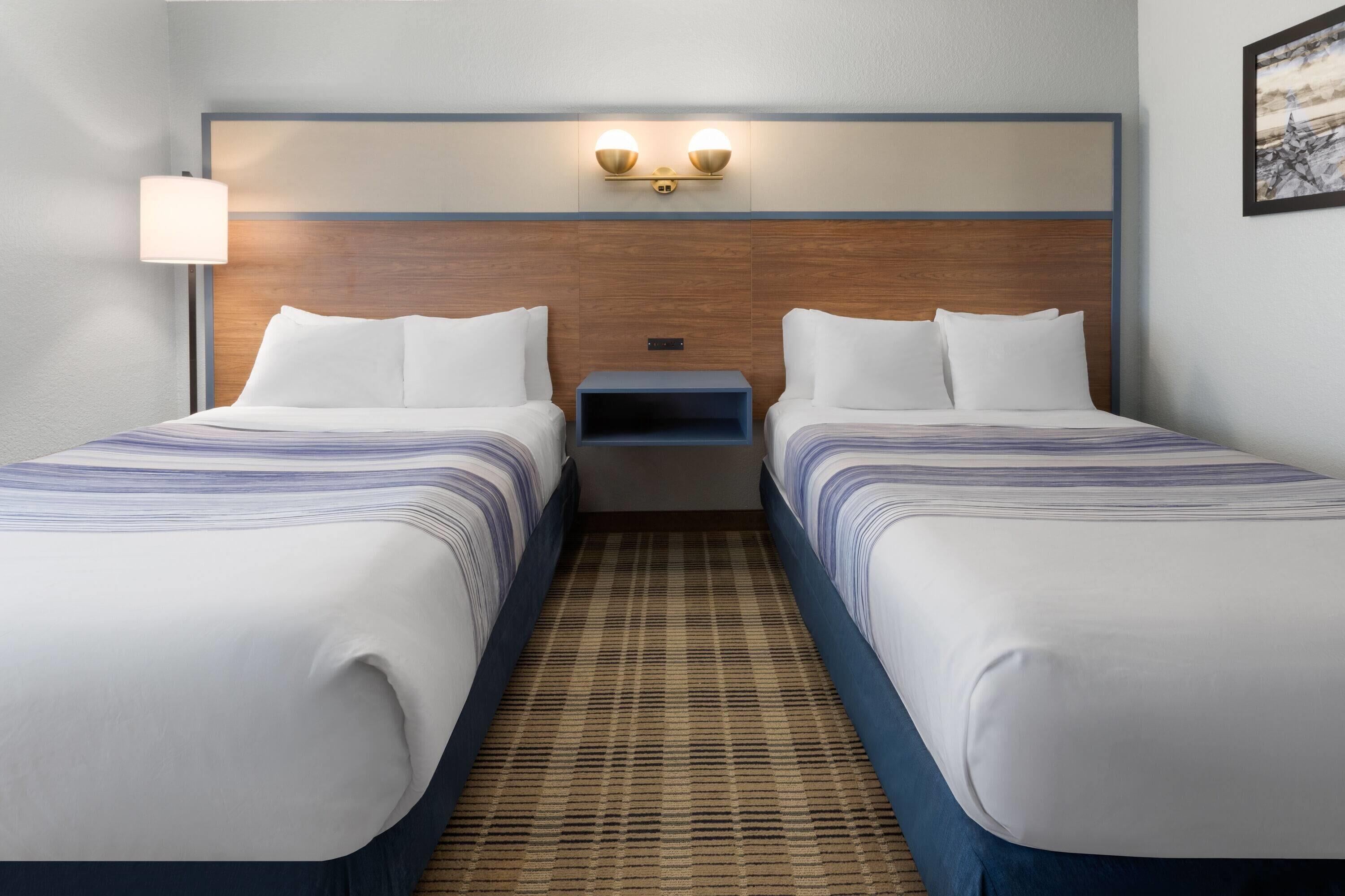 Une chambre d’hôtel avec deux lits, une table de chevet et un luminaire fixé au mur.