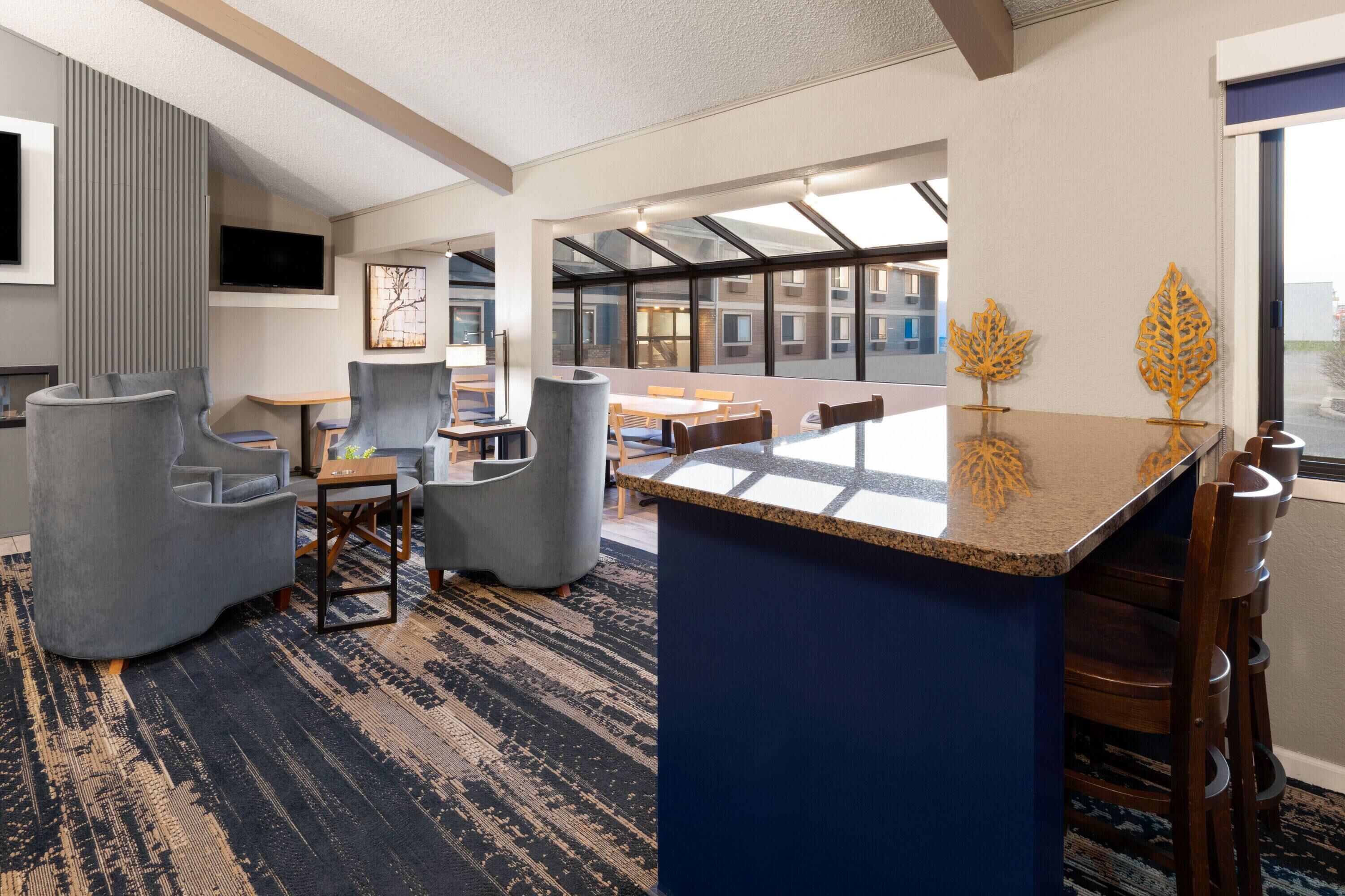 Una hall d'hotel moderna con un'area bar centrale, diverse disposizioni di posti a sedere e ampie finestre che offrono vista sulla città.