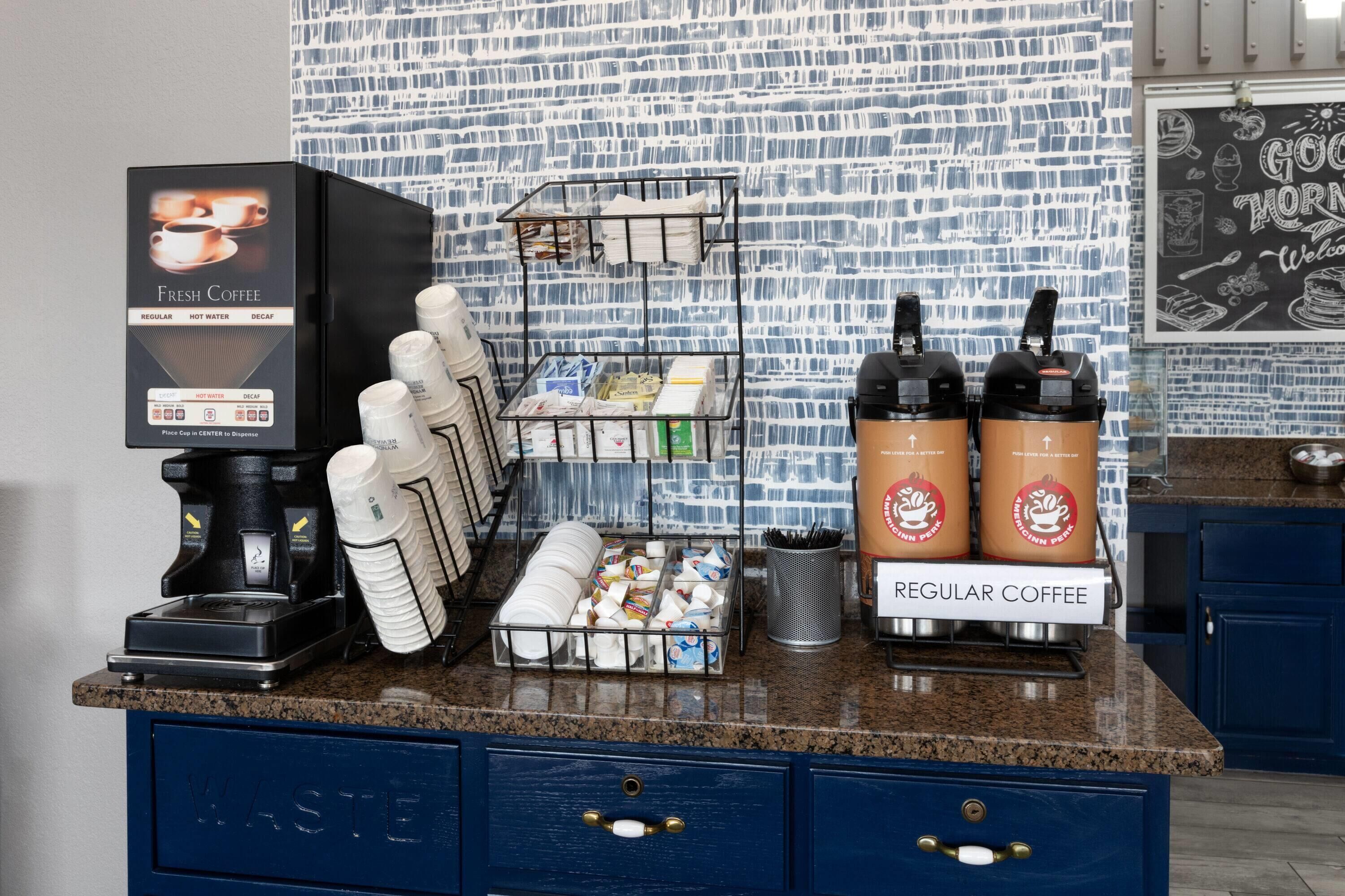 Een koffiehoek met een koffieapparaat, wegwerpbekers en een koffieautomaat.