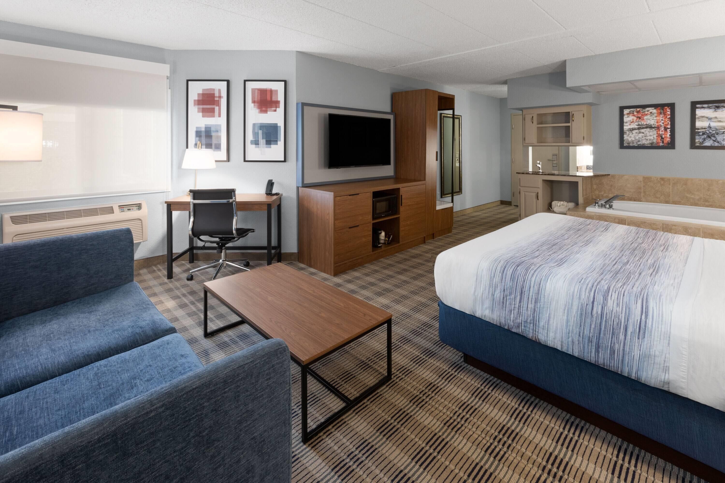 A hotel room with a large bed, a desk with a chair, a TV, a bathroom, and artwork on the walls.