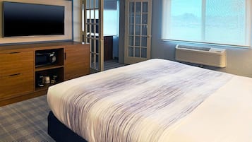 Ein Hotelzimmer mit einem großen Bett, einem flachbildfernseher an der Wand, einem begehbaren Kleiderschrank und einem Fenster mit Ausblick.