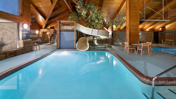 An indoor swimming pool with a slide, wooden interior, and seating area.