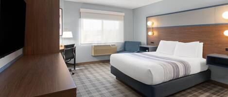 Une chambre d’hôtel avec un grand lit, un bureau, une télévision et une fenêtre avec des stores.