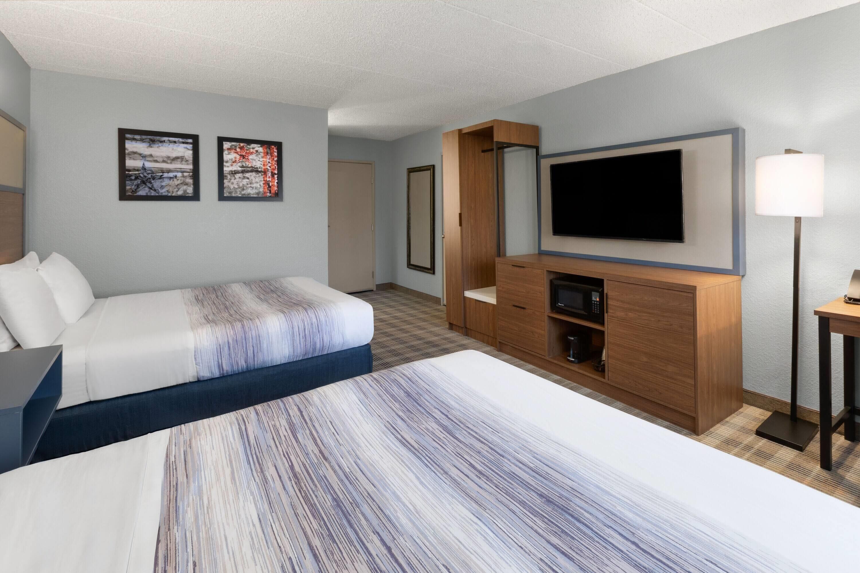 Habitación de hotel con una cama grande, televisión montada en la pared, un armario de madera y una mesita de noche.