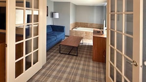 A room with a sofa, a small table, a bathroom with a bathtub, and a window.