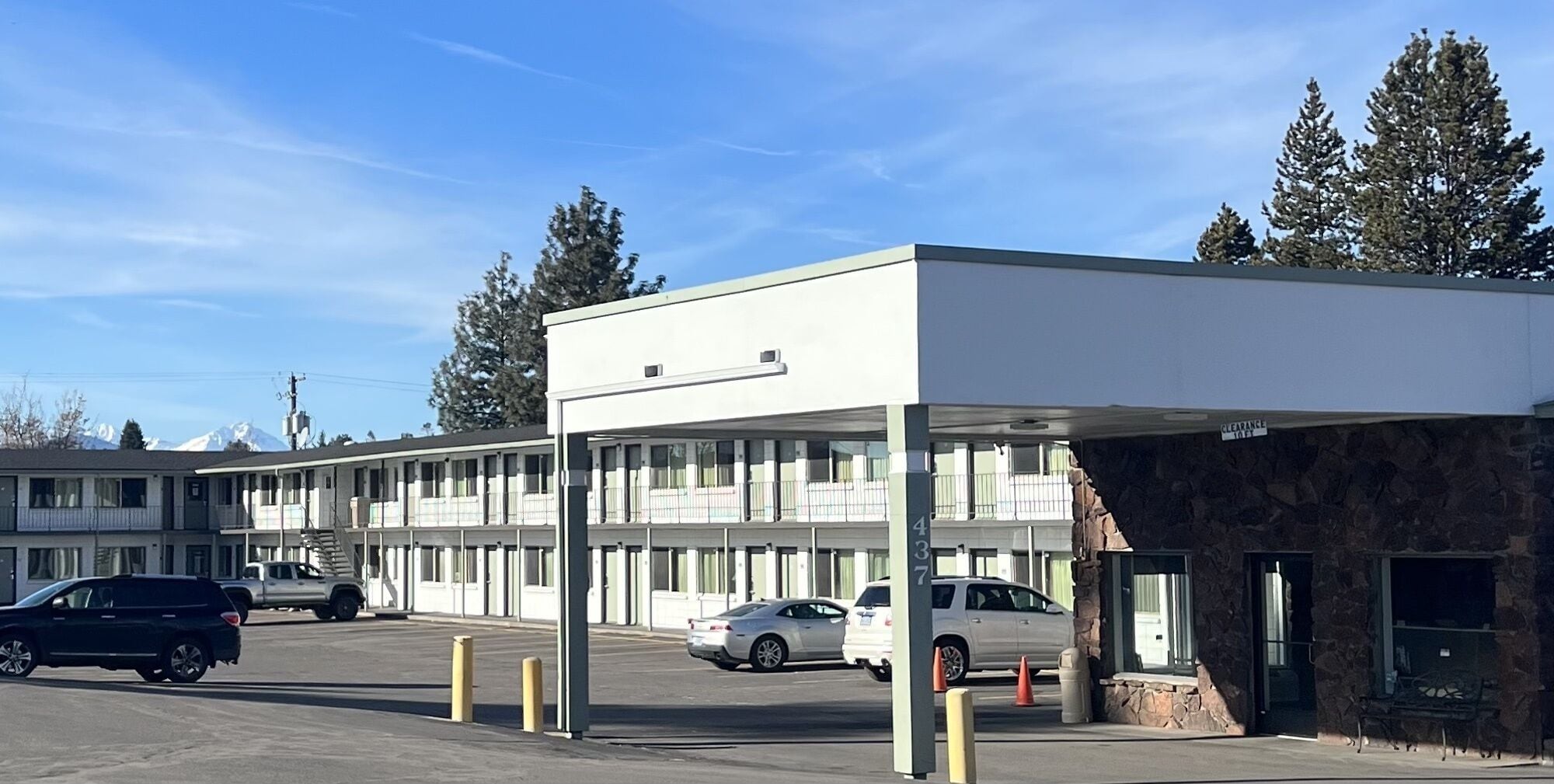 Un motel doté d’un parking couvert, d’une entrée avec une façade en pierre et d’une rangée de chambres avec balcon.