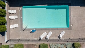 An aerial view of a rectangular swimming pool with a tiled deck, surrounded by lounge chairs and a poolside area. - Bend Inn & Suites (Bend)