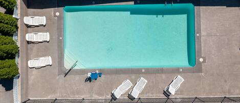 Vue aérienne d’une piscine rectangulaire dont le bord est recouvert de carreaux, entourée de chaises longues et d’un espace aménagé au bord de la piscine.