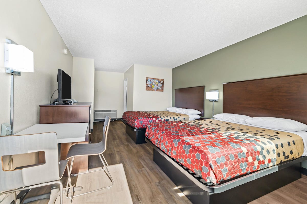 A hotel room with two beds, a desk, a chair, a television, and a painting on the wall.