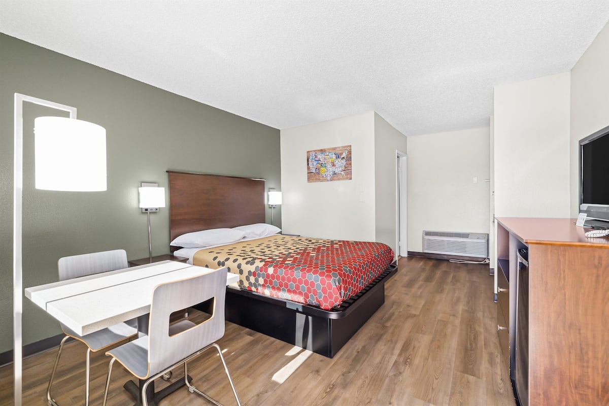 A hotel room with a bed, a desk, a chair, a TV, and a heater.