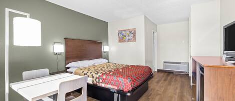 A hotel room with a bed, a desk, a chair, a TV, and a heater.