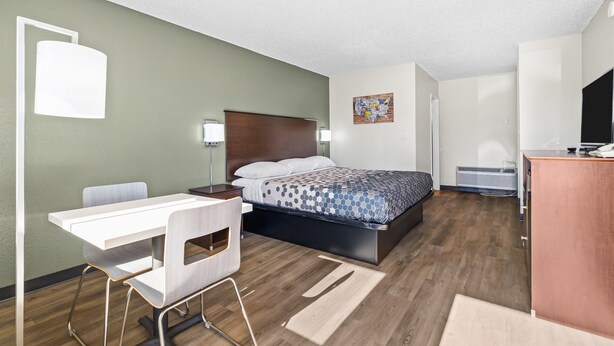 A modern hotel room with a bed, desk, chair, and a small kitchenette.